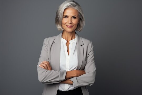 Confident mature businesswoman standing with arms crossed against grey background.