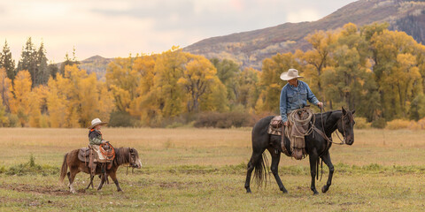 Father and son cowboys on horse and pony riding in the colorful mountains