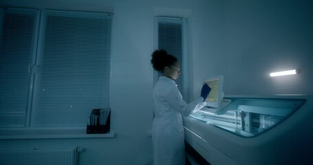 Work in a medical laboratory. A woman in a lab coat, disposable gloves and safety glasses sets up a blood splitting device using a screen