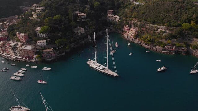 Aerial drone shot of a big sailing yacht staying in a bay near Portofino in Italy surrounded by cliffs and cliffs with Italian-style houses