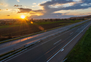 Cars drive at high speed on the highway through the rural landscape. Fast blurred highway driving. A scene of speeding on the highway. Beautiful sunset in the background.