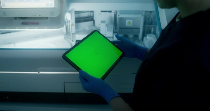A man in a lab coat and disposable gloves uses a tablet with a green screen standing in a medical laboratory, close-up of his hands, an unrecognizable person