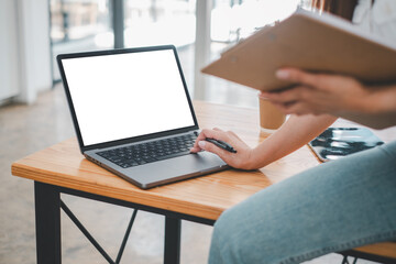 Fototapeta premium Close-up of a professional's hands at a modern workstation, featuring a laptop with a blank screen ready for customization, alongside a clipboard and a smartphone.