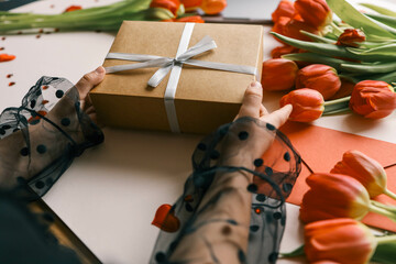 Gift box with a bow and tulips in the hands of a girl, festive background