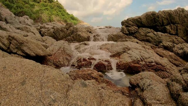 January 14, 2024 - Nai Harn, Phuket Thailand. A small waterfall that appears from thin air when it becomes flooded by high tide in the ocean and waves crashing into the rock from the opposite side.