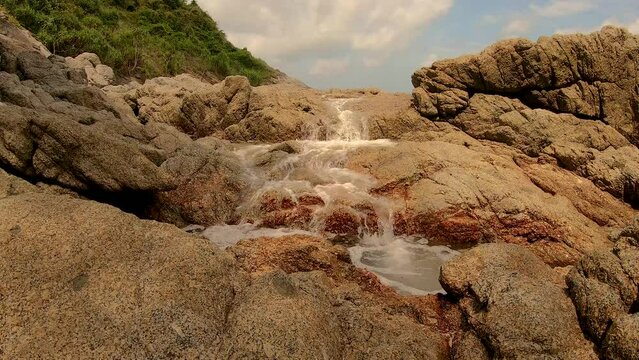 January 14, 2024 - Nai Harn, Phuket Thailand. A small waterfall that appears from thin air when it becomes flooded by high tide in the ocean and waves crashing into the rock from the opposite side.