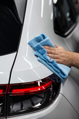 A mechanic wipes the body of a white car with a microfiber cloth. 
