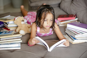 Pausa para Imaginar Criança deitada Entre Contos e Fábulas lendo livros no sofá.