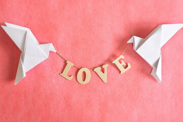 Spread message of love concept. Two white dove origami carrying word LOVE on red background.