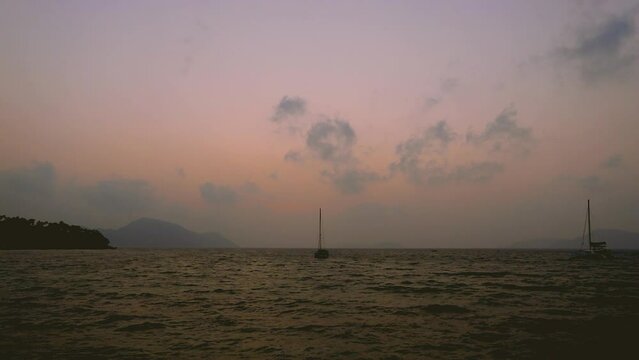 February 1, 2024 - Rawai, Phuket Thailand. Time lapse of sunrise viewed from the landing pier with sailboats anchored in the water.