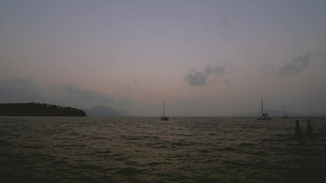 February 1, 2024 - Rawai, Phuket Thailand. Time lapse of sunrise viewed from the landing pier with sailboats anchored in the water.