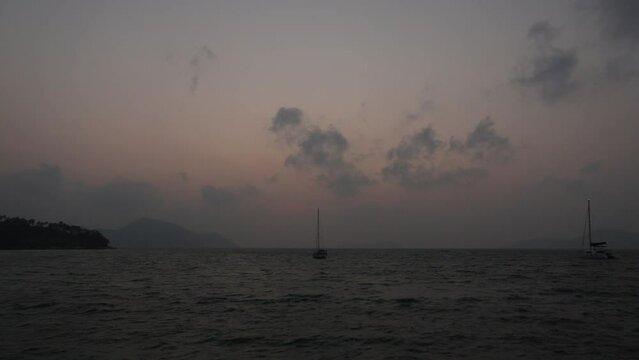 February 1, 2024 - Rawai, Phuket Thailand. Sunrise viewed from the landing pier with sailboats anchored in the water.
