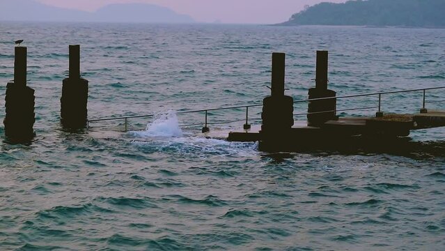 February 1, 2024 - Rawai, Phuket Thailand. Slow motion of small waves gently crashing into the landing pier steps in early morning.