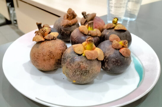 Mangosteen (Garcinia mangostana), also known as the purple mangosteen, Clusiaceae family. Group of mangosteen fruit on white plate. Selective focus.
