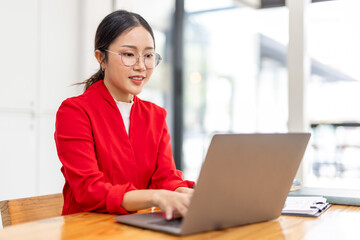 Portrait of Happy young business asian woman in red suit sitting at her desk in the office business finance concept.	