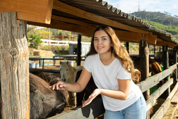 Portrait of smiling woman next to pony in stall at a livestock farm