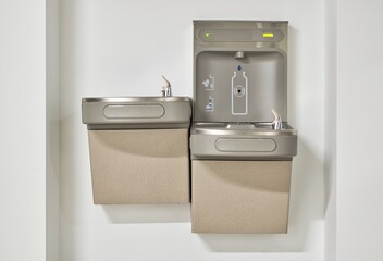 Water bottle refilling station with twin drinking fountains isolated by a plain white wall. Touchless automated eco friendly technology.