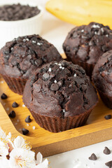 Dark chocolate chip muffins with bananas on a wooden plate. Healthy sweet vegan dessert or snack. Close-up.