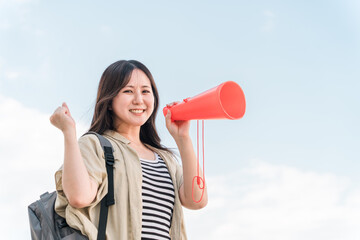 青空の下でメガホンで応援・声援・エールを送る若いアジア人女性
