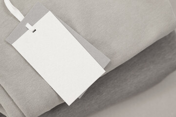 Garment with cardboard tag on beige background, closeup. Space for text
