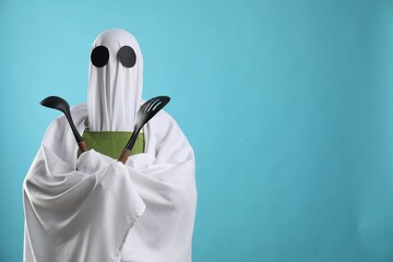 Woman in ghost costume and apron with kitchen set on light blue background, space for text