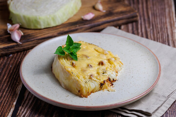 Homemade grilled cabbage steaks with cheese. Healthy vegetarian food ready to eat on a serving plate, cutlery. Wooden table background, close up
