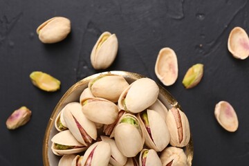 Tasty pistachios in bowl on black table, top view