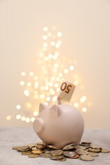 Piggy bank with euro banknote and coins on grey table against blurred lights, space for text