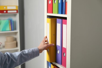 Woman taking binder office folder from shelving unit indoors, closeup