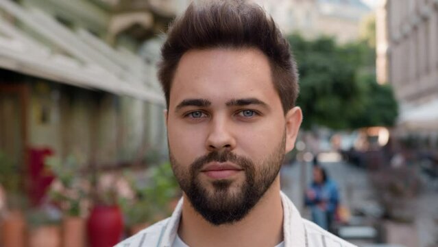 Close up portrait European Caucasian young man looking at camera business city outside street businessman gen z male face beard handsome guy standing posing urban model calm focused serious expression