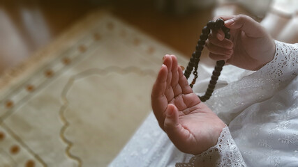 High angle photo shoot of moslem woman's hands praying and holding a prayer beads, sitting down on...