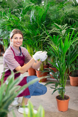 Adult female saleswoman in uniform with areca pot in plant store