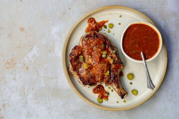 Grilled pork chop with tangy sauce with gerkin garnish, a bistro classic presented as an overhead, landscape shot with negative space. Minimalist style on a white plate.