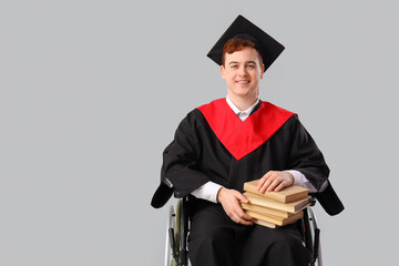 Male graduate in wheelchair with books on light background