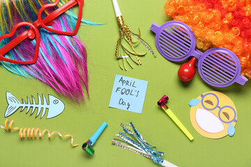 Colorful wigs with funny glasses, party whistles and sticky note on green background. April Fools...