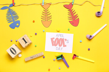 April Fool's Day card with calendar, paper fishes and party whistles on yellow background