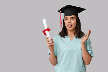 Surprised female medical student in graduation hat with diploma on white background