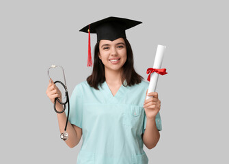 Happy female medical student in graduation hat with stethoscope and diploma on white background