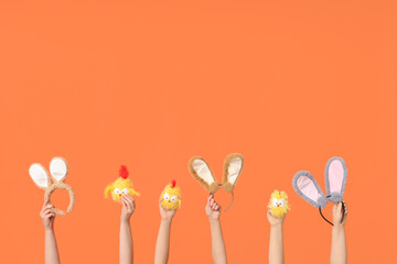 Female hands holding Easter bunny ears headbands with toy chickens on orange background