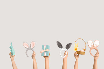 Female hands holding Easter bunny ears headbands with gift box, toy rabbit and basket on white background
