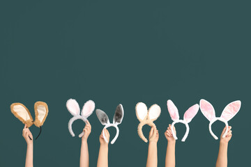 Female hands holding Easter bunny ears headbands on dark green background