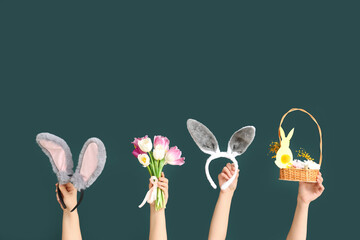 Female hands holding Easter bunny ears headbands with basket and tulips on dark green background