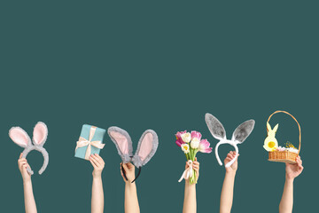 Female hands holding Easter bunny ears headbands with gift box, basket and tulips on dark green...