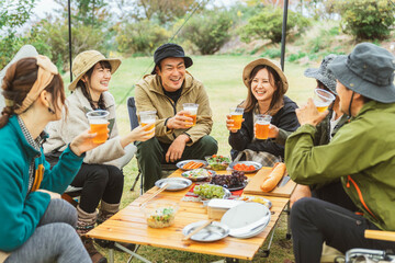 キャンプ・デイキャンプ・グループキャンプでビールを飲みながら談笑する男女キャンパー
