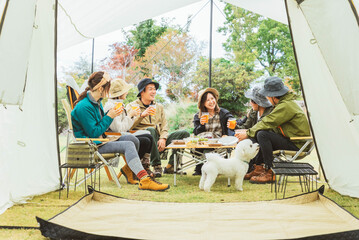 秋冬のキャンプ場で仲間と一緒にビールを飲んでパーティーするアジア人の男女（グルキャン）
