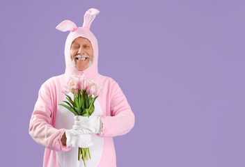 Senior man in Easter bunny costume with bouquet of tulip flowers on lilac background