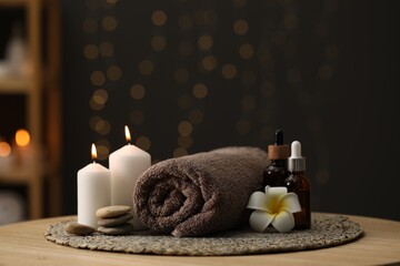 Fototapeta na wymiar Spa composition. Rolled towel, cosmetic products, stones, burning candles and plumeria flower on table indoors. Space for text