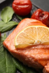 Tasty grilled salmon with lemon, spinach and tomatoes on table, closeup