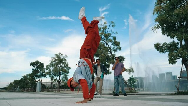 Asian skilled hipster doing freeze pose at camera surrounded by break dancer team near fountain with sky background. Group of handsome people practice b-boy dance. Outdoor sport 2024. Sprightly.