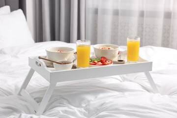 Tray with tasty breakfast on bed at home